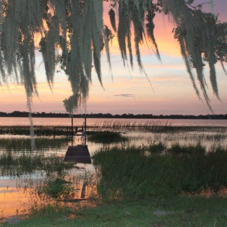 A serene image of Lake Letta at sunset, surrounded by lush greenery, representing the peaceful and scenic atmosphere at Lake Letta RV Park in Avon Park, FL.